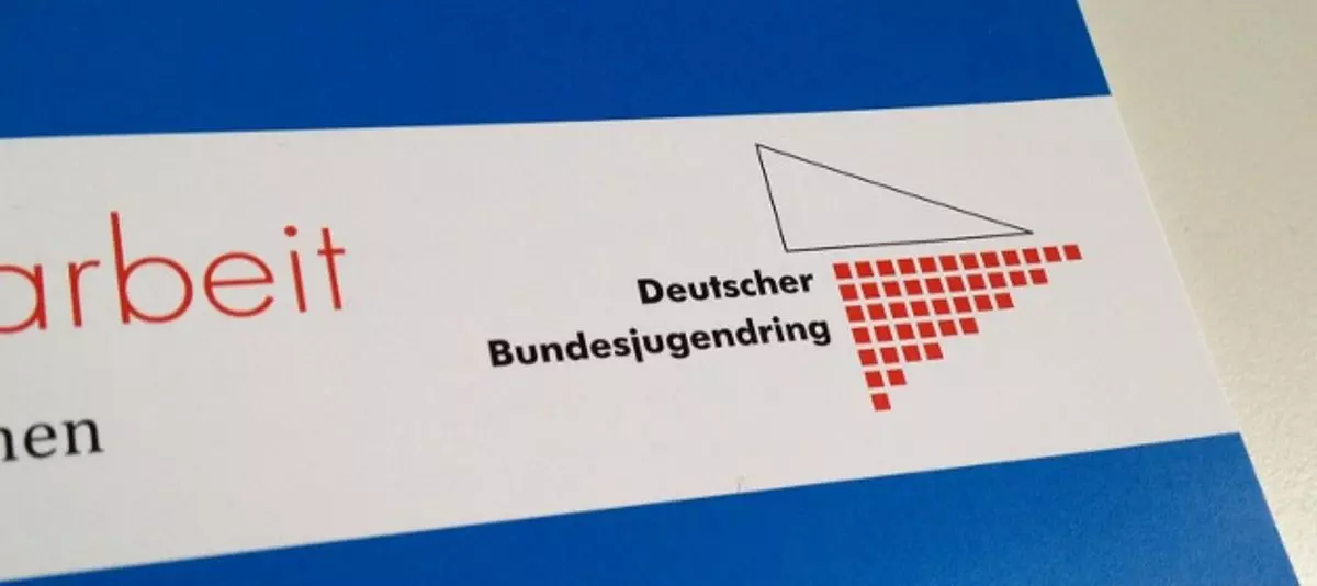 Ein Ausschnitt von einem Buch, auf dem steht: "Deutscher Bundesjugendring". Daneben zu sehen ist eine schwarze Umrandung eines Dreiecks + ein rotes umgedrehtes Dreieck, bestehend aus kleinen Würfeln.